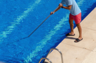 Man cleaning the swimming pool with a telescopic pole